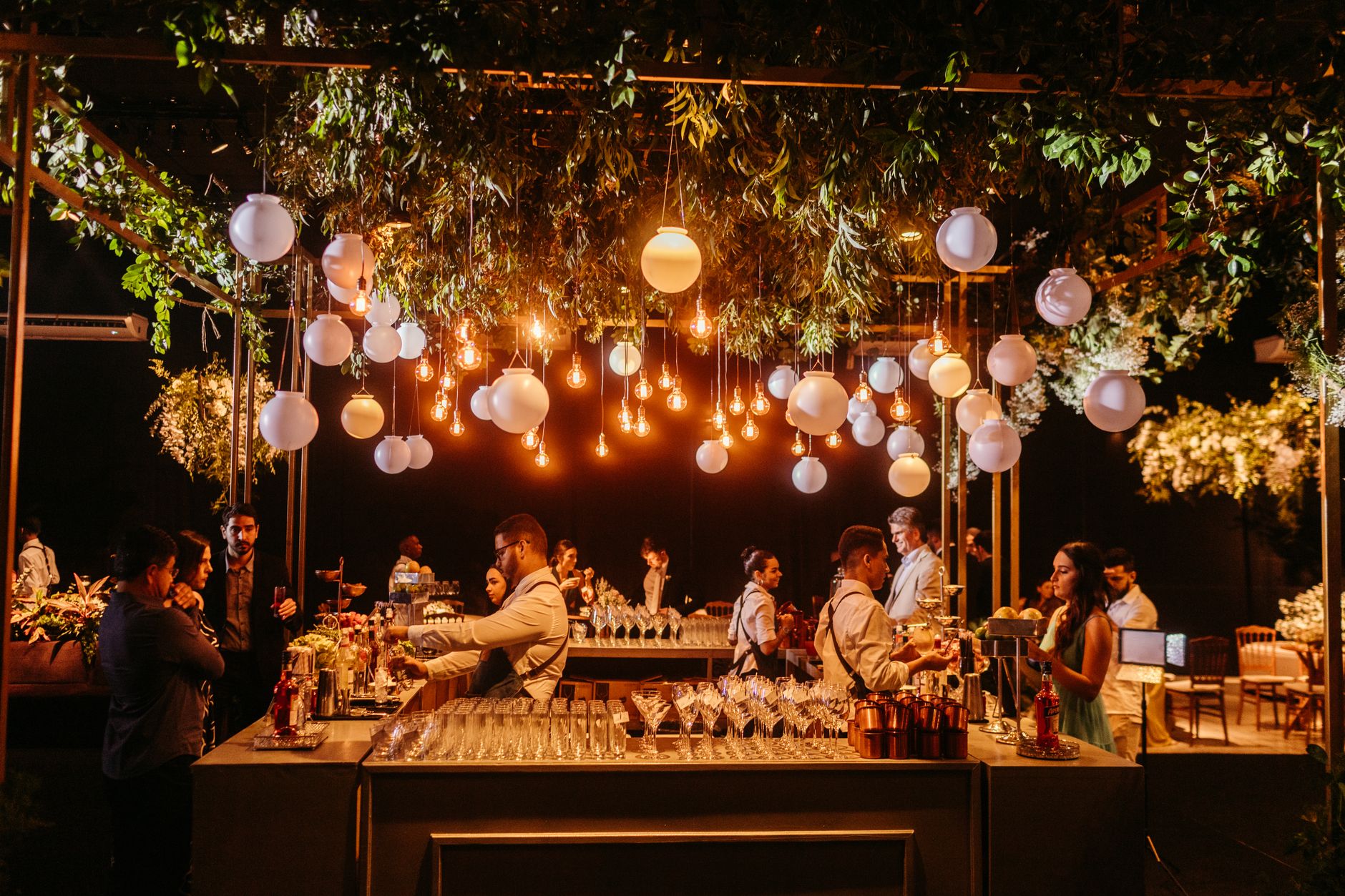 A stylish wedding reception showcasing a beautifully decorated bar with ambient lighting and lush greenery.